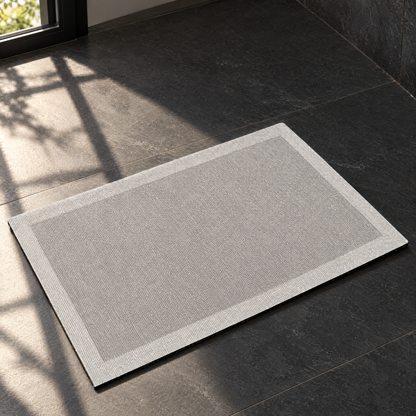 Light grey quick-dry bath mat on a sunlit dark slate bathroom floor