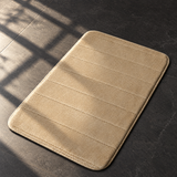 Khaki plush anti-slip bath mat on a sunlit dark stone bathroom floor