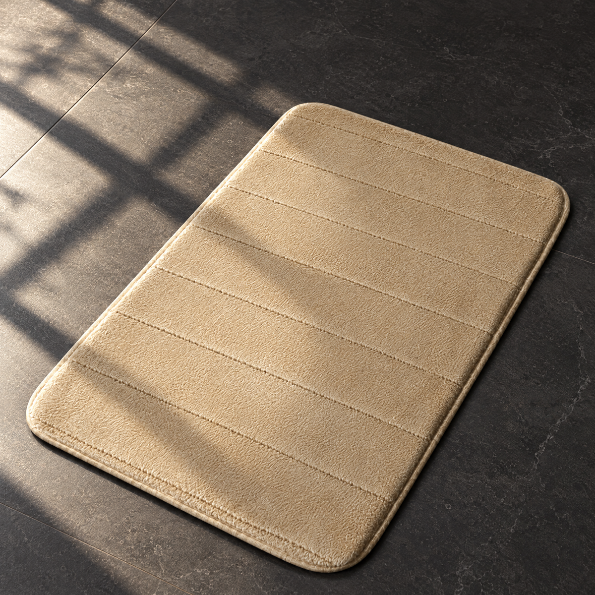 Khaki plush anti-slip bath mat on a sunlit dark stone bathroom floor
