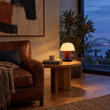 Red mushroom table lamp glowing beside a leather armchair at dusk
