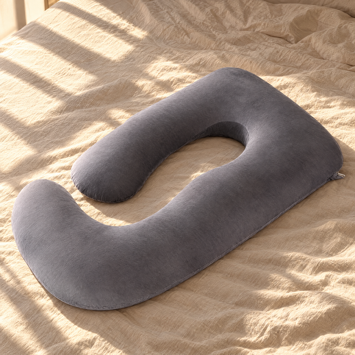 Grey U-shape pregnancy pillow on sunlit oat linen bedding