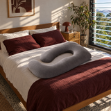 Grey U-shape pregnancy pillow on a guest bedroom bed