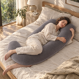 Woman side-sleeping with a grey U-shape body pillow between her knees on a linen bed