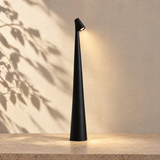 Black Aften cordless LED table lamp glowing against a sunlit plaster wall