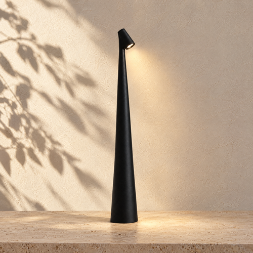 Black Aften cordless LED table lamp glowing against a sunlit plaster wall