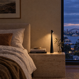 Black cordless LED table lamp on a bedside table at dusk