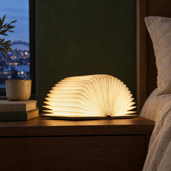 Lumibook foldable book lamp with wood covers glowing on a bedside table